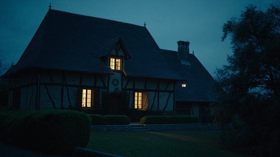 Maison ancienne éclairée de l'intérieur à la tombée de la nuit, hautes toitures sombres