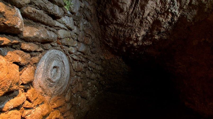 Meule de pierre encastrée dans un mur de moellons, en lumière rasante