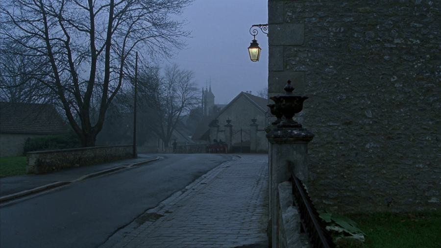 Rue de village dans la brume au petit matin, lanterne allumée et clocher au fond