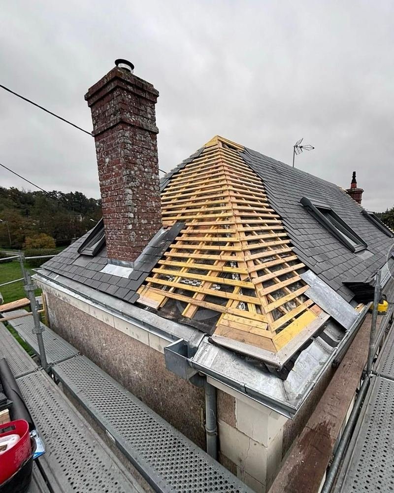 Croupe de toiture en cours de liteaunage autour d'une souche de cheminée en brique, vue de l'échafaudage