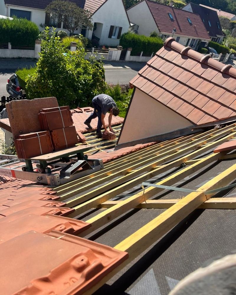 Tuiles neuves en terre cuite réparties par paquets sur un versant en cours de couverture